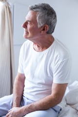 Thoughtful senior man sitting on bed in bedroom