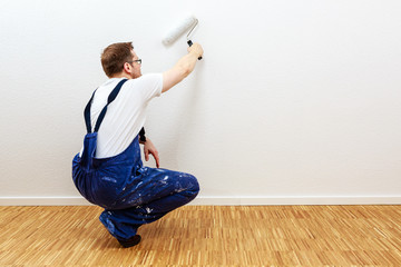 Mann im Blaumann streicht eine Wand weiß an