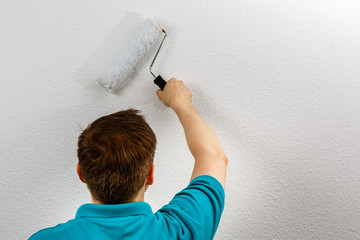 Mann streicht Wand weiss an, closeup