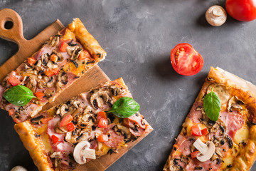 a slice of square pizza with basil tomatoes and mushrooms on a wooden board. Top view. Copyspace. Pizza on the gray table