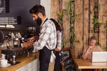 Waiters using a coffee machine and customer on a laptop
