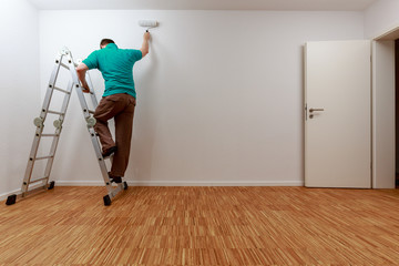 Mann auf Leiter beim Streichen der Wand