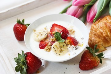 Breakfast in bed with Yogurt berry bowl crissant and tulips flowers in a tray, selective focus