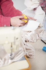 Female tailor cutting piece of cloth at table in fashion studio