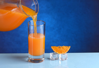 versare succo di arancia nel bicchiere di vetro - sfondo blu