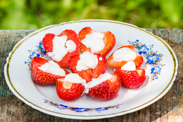 Halves strawberries poured cream in plate, outdoors.
