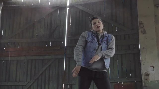 Active young female dancing freestyle in an abandoned building. She is wearing a grey hoodie and pinup hair scarf on an old wooden door and smoky background. 