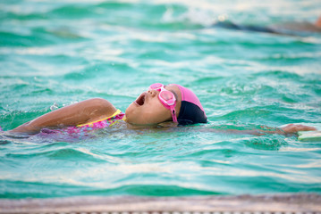 Fototapeta na wymiar Little cute girls deftly swim in pool