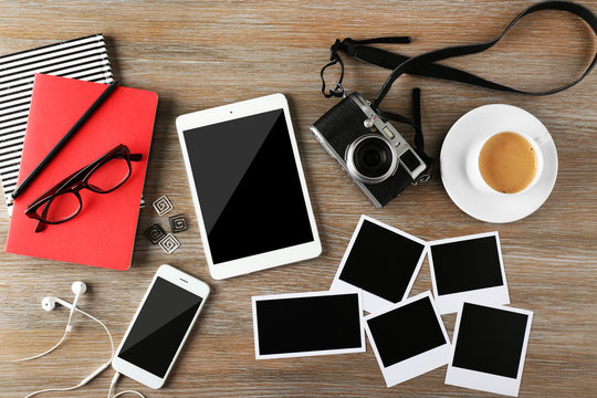 Tablet, phone, photos and cup of coffee on a wooden desk background, top view