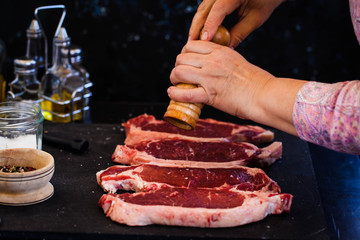 Hand Sprinkled raw beef steaks with pepper ready to prepare bbq. 