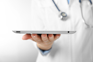 Professional doctor with tablet on light background