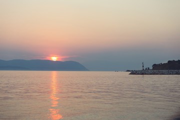 Sunset falling behind mountains is viewed from a beach on greek island
