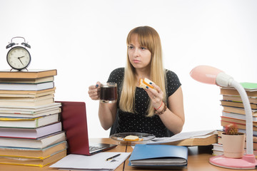 Hungry young teacher sitting wearily with a sandwich and coffee