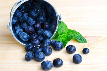 Fresh blueberries with mint in metal bucket on wooden  background