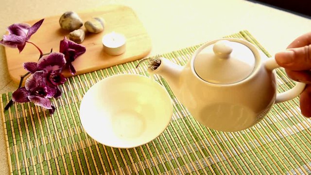 Tea ceremony. Green tea is poured from a teapot into a cup on a light background. Slow motion