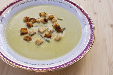 Fresh asparagus cream soup on wooden background overhead shoot. Served with a white bread croutons roasted on the butter and with a green asparagus heads. Soup in old vintage deep plate. 
