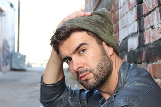 Fashionable hipster man touching his head with his hand. Young man with modern beanie looking down and thinking about something outdoors.
