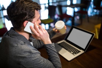 Man holding disposable coffee cup while talking on mobile phone