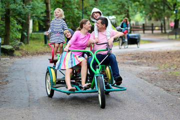 Happy family of 5 riding ricksha bike in vacation park. Father, mother and kids enjoying time together outdoors during summer holidays.