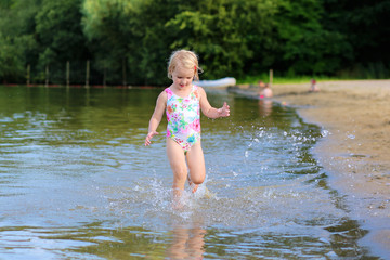 Happy kid playing in the lake. Healthy smiling toddler girl enjoying summer vacation outdoors.