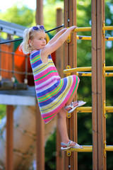 Fototapeta premium Happy kid having fun at playground. Adorable little child, blond cute toddler girl, enjoying active summer vacation outdoors playing in the park on a sunny day.