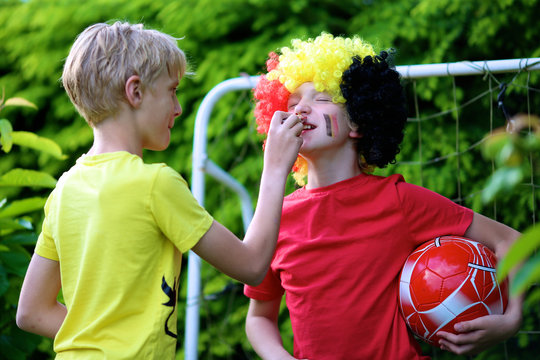 Happy young belgian boys having fun supporting Red Devils during european football championship EURO 2016. Kids in Belgian national tricolour painting flags on their face and playing soccer outdoors.
