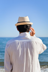 Person talking on cell phone walking by open water blue sky horizon, sunlight outdoors.