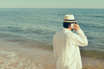 Back view of man talking holding mobile phone, blue sky sea outdoors background