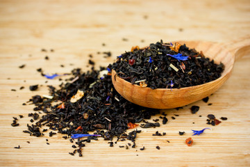 Dry tea in spoon on wooden background close up