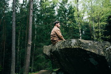 bearded man tourist hipster sits on rock and dream in mountain green forest