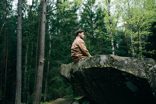 bearded man tourist hipster sits on rock and dream in mountain green forest