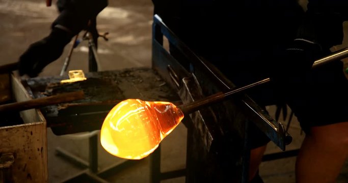 Skilled glass blower shaping and moulding large glob of molten glass
