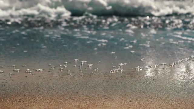 Slow motion close up of waves lapping on red sand beach focus in FG