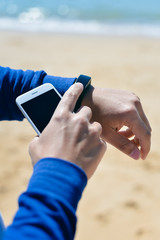 Person holding phone checking connection using smart watch on the sandy beach. Sunny background outdoors