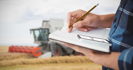 Farmer with pencil on book against a harvester