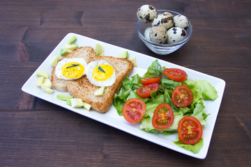 Toast with quail eggs and salad on a wooden table