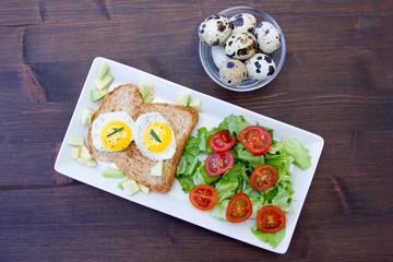 Toast with quail eggs and salad on a wooden table seen from above
