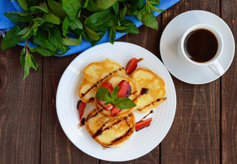 Rustic pancakes with fresh strawberries and chocolate on a white plate and cup of coffee. The top view