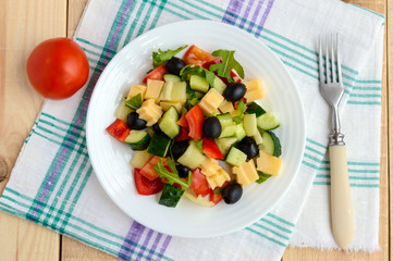 Fresh diet salad with cucumbers, tomatoes, olives cheese, bell peppers, arugula on a light wooden background. The top view