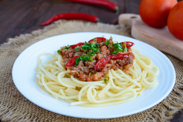 Spaghetti Bolognese with chili on a white plate on a wooden background. Close up