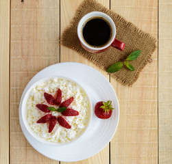 Homemade cottage cheese with fresh strawberries, mint leaves decoration in a white bowl and a cup of coffee. Useful eco breakfast. Healthy eating.
