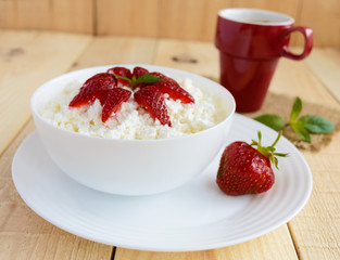 Homemade cottage cheese with fresh strawberries, mint leaves decoration in a white bowl and a cup of coffee. Useful eco breakfast. Healthy eating.