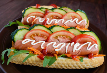 Home made hot dogs with vegetables, juicy sausage and arugula on the wooden background. Close-up.