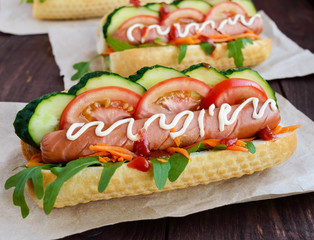Home made hot dogs with vegetables, juicy sausage and arugula on the wooden background. Close-up.