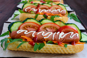 Home made hot dogs with vegetables, juicy sausage and arugula on the wooden background. Close-up.