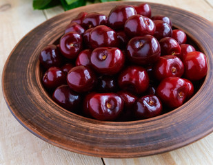 Ripe black cherries in a clay bowl on a light wooden background. Close-up.