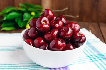 Ripe black cherries in a white bowl on a light background. Close-up.