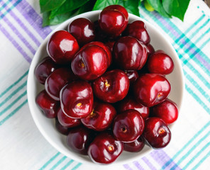 Ripe black cherries in a white bowl on a light background. The top view