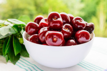Ripe black cherries in a white bowl on a background of nature. Close-up.