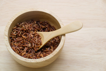 Brown rice,in a wooden bowl with wooden spoon  on wood backgroun